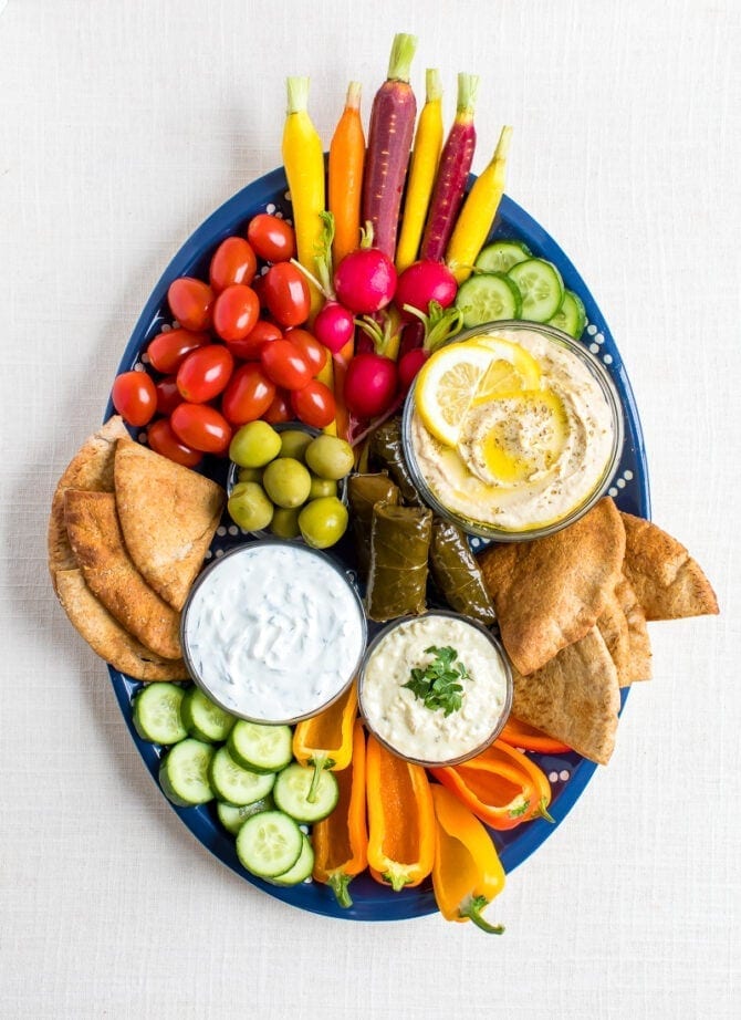 Vegetarian mezze platter with carrots, radishes, tomatoes, cucumber slices, green olives, domades, pita chips, peppers and a variety of hummus and dips.