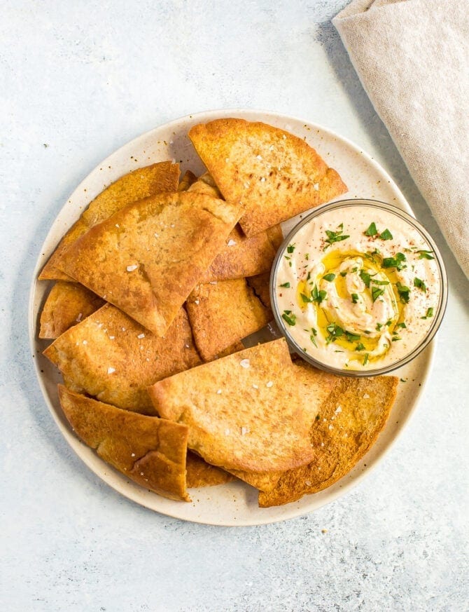 Baked pita chips on a plate with hummus.