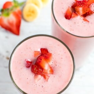 Two strawberry banana smoothies topped with chopped strawberries.