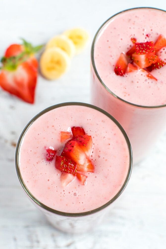 Two strawberry banana smoothies topped with chopped strawberries.