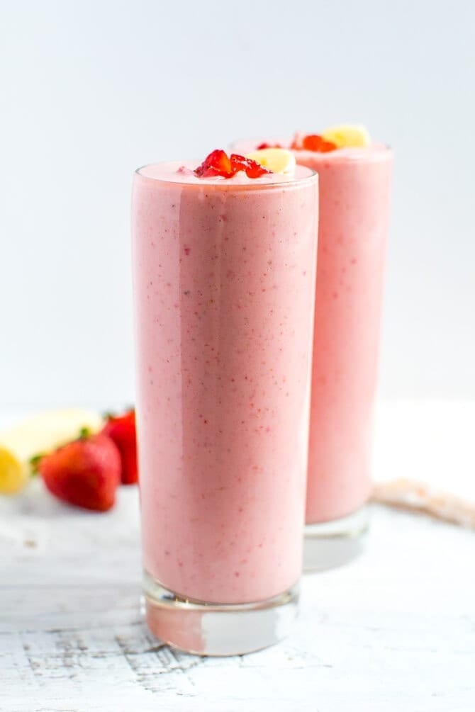 Two glasses full of strawberry banana smoothies topped with slices of banana and chopped strawberries.