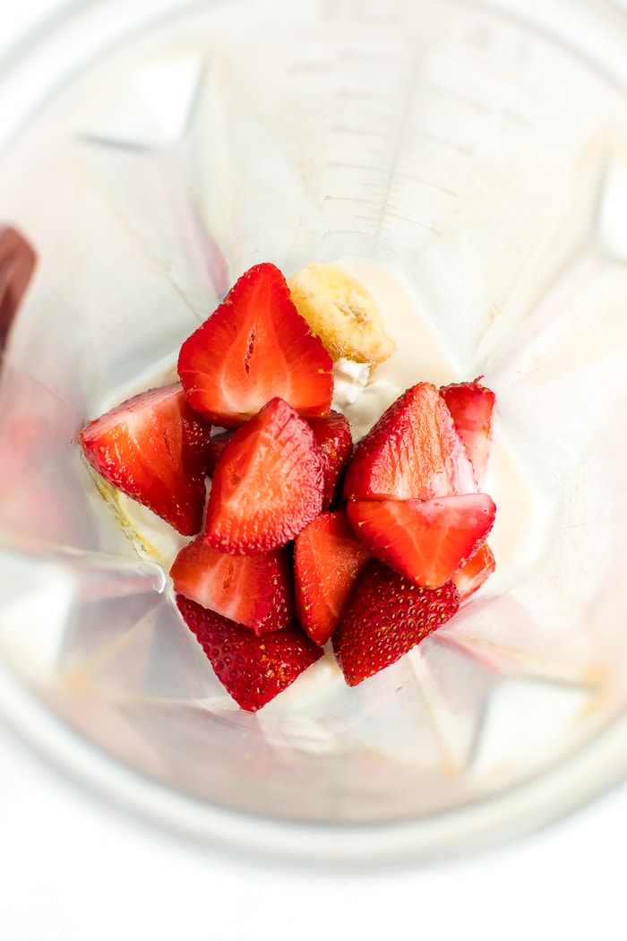 Strawberries, frozen banana, almond milk, honey, and greek yogurt in a blender.