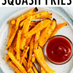 Plate of butternut squash fries topped with salt and served with ketchup.