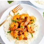 Plate of cauliflower cheese grits topped with blackened shrimp and chipped fresh parsley. A fork is resting on the plate.