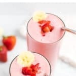 Two strawberry banana smoothies with a silver straw and topped with a banana slice and chopped strawberries.