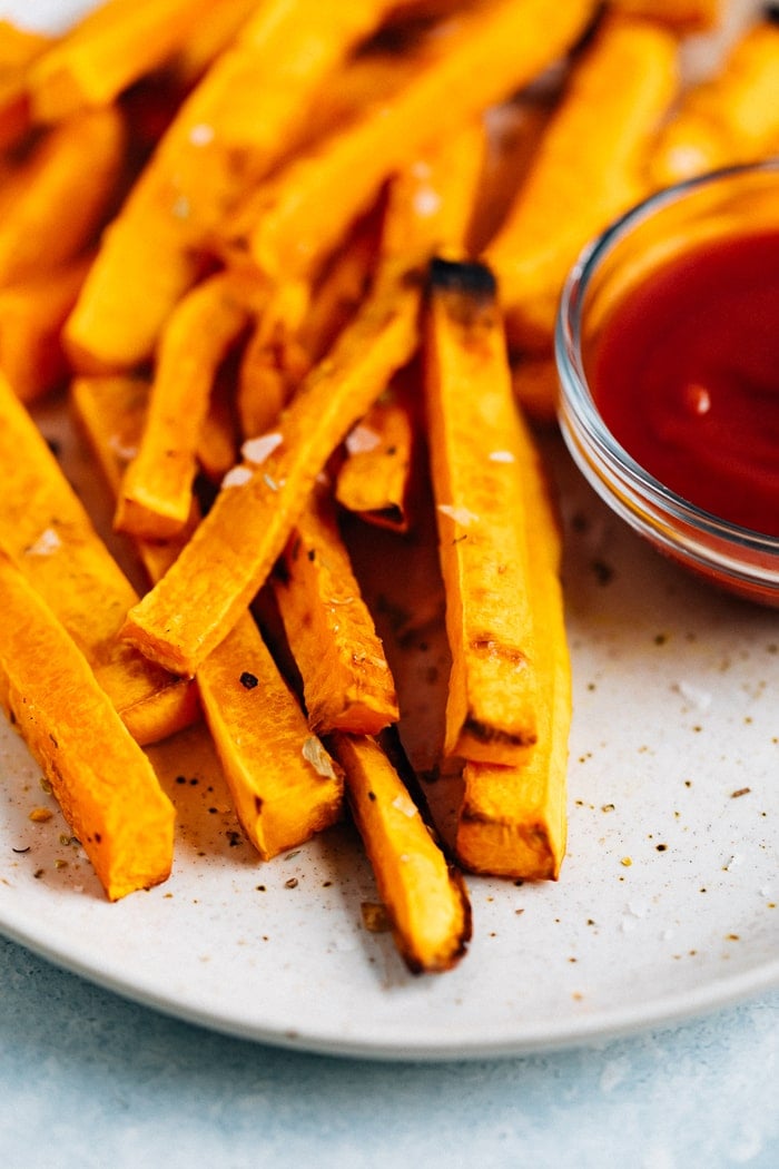 Plate of butternut squash fries topped with salt and served with ketchup.