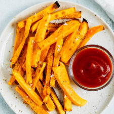 Butternut squash fries on a plate with a bowl of ketchup.