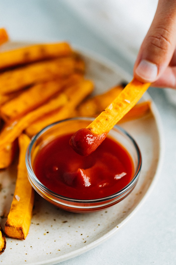 Hand dipping a butternut squash fry in ketchup.