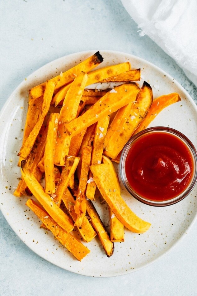 Butternut squash fries on a plate with a bowl of ketchup.