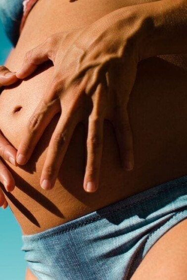 Pregnant woman wearing a blue bikini and holding her stomach.