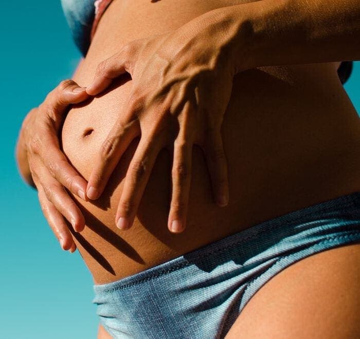 Pregnant woman wearing a blue bikini and holding her stomach.