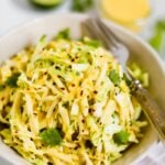 Close up photo of a bowl of mango jicama slaw topped with a mango dressing, red pepper flakes, and cilantro.