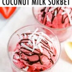 Two glasses with a scoop of strawberry coconut milk sorbet drizzled with chocolate and coconut flakes. Two spoons and strawberries are to the side.
