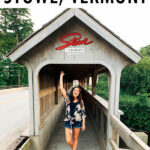 Woman standing and waving under a covered bridge that has a Stowe Vermont sign on the top.