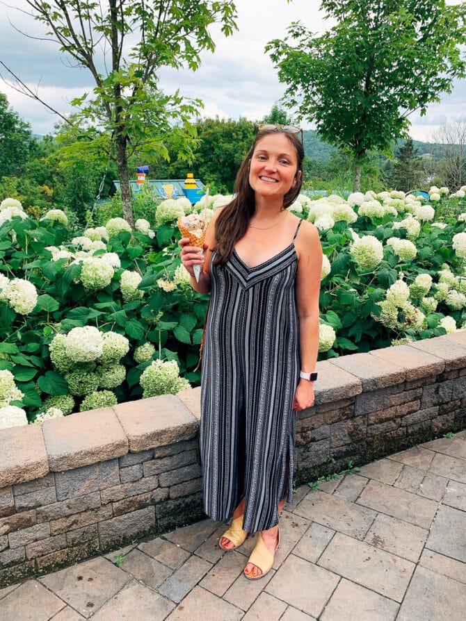 Woman in a jumpsuit standing in front of a bed of hydrangeas and holding a cone of Ben & Jerry's ice cream.