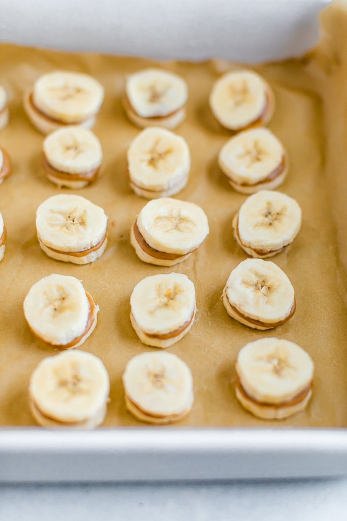 Slices of banana sandwiched with peanut butter on a tray lined with parchment paper.