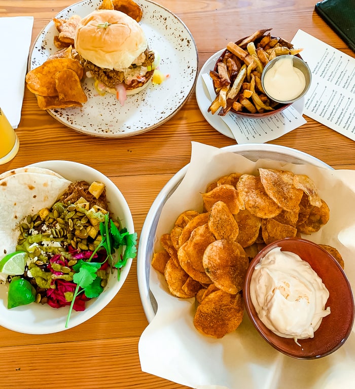 Restaurant table with an assortment of food plates including a sandwich, homemade chips and dip, french fries, and tortillas with dip.