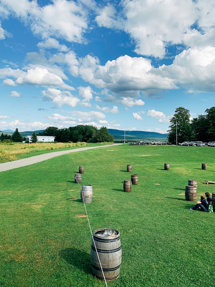 View of a brewery with open land, barrels, and trees and mountains in view.