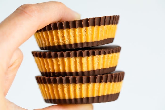 Hand holding three homemade peanut butter cups with layers of chocolate and peanut butter.