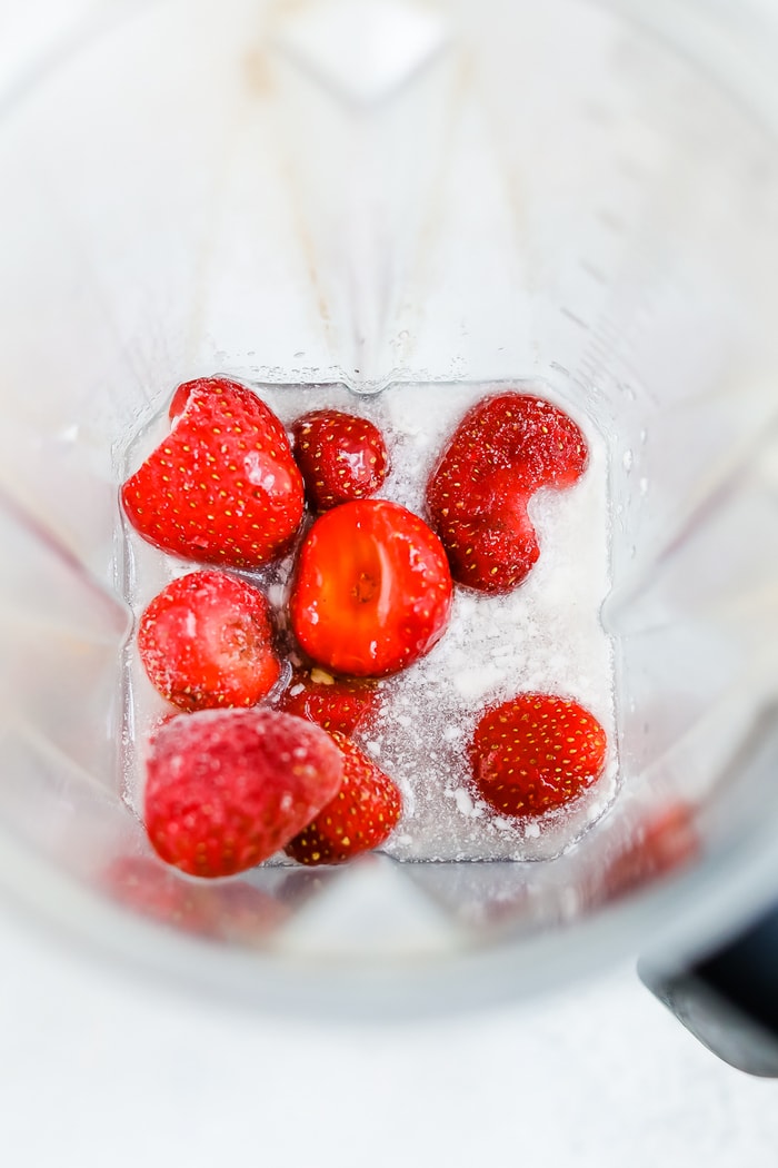 Ingredients for strawberry coconut sorbet in a blender, frozen strawberries, a can of coconut milk, and maple syrup.