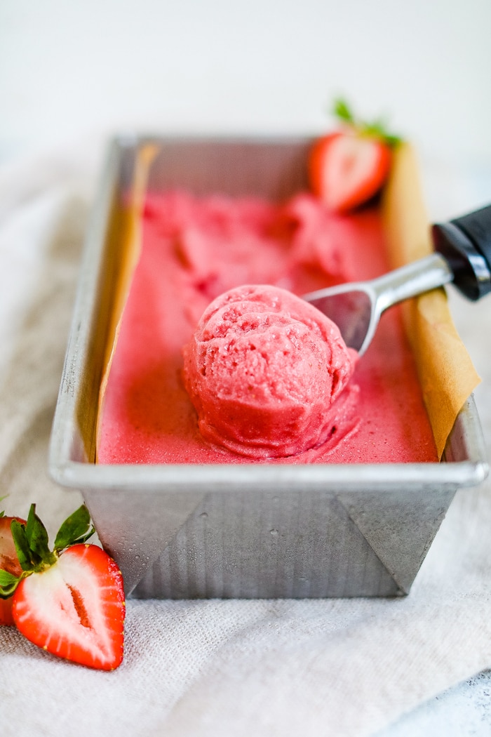 A ice cream scooper scooping strawberry coconut sorbet.