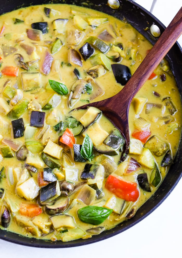 Skillet with vegetable curry in a coconut curry sauce. A wood spoon is in the skillet.