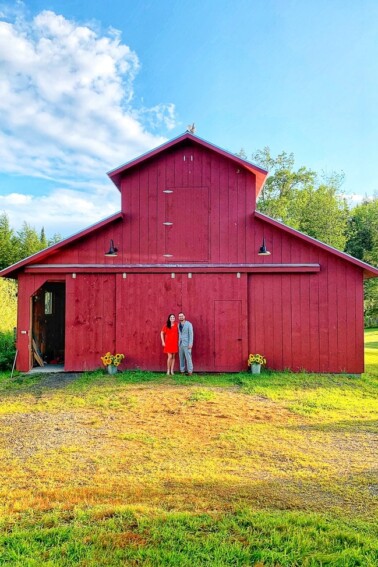 A couple standing outside of a red barn.