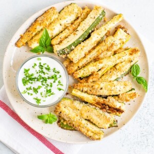 Plate of crispy zucchini fries on a plate with a creamy dip topped with chopped parsley.