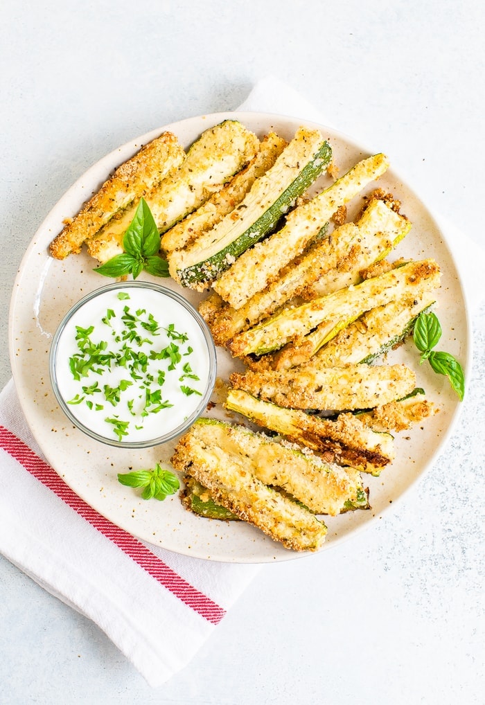 Plate of crispy zucchini fries on a plate with a creamy dip topped with chopped parsley.