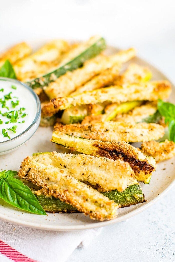 Plate of crispy zucchini fries on a plate with a creamy dip topped with chopped parsley.