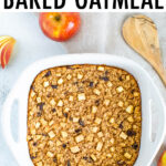 Dish of apple cinnamon baked oatmeal filled with raisins and chunks of apples. Apples and a wooden spoon are around the dish.