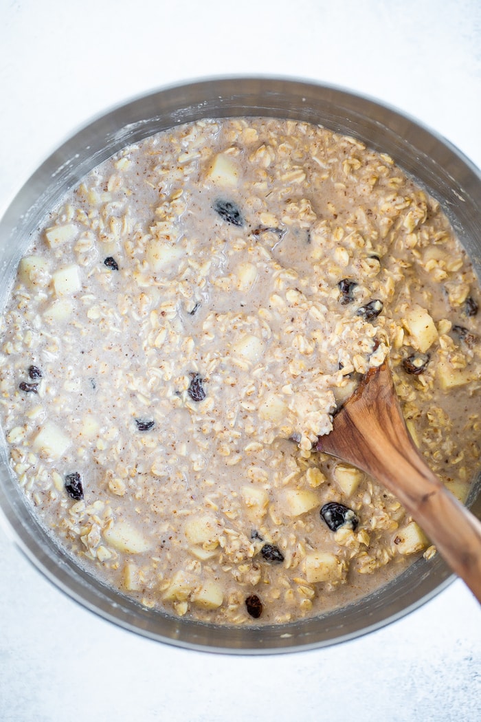 Wood spoon mixing the mixture for apple cinnamon baked oatmeal in a mixing bowl.