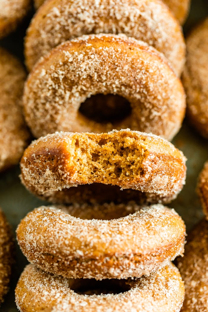 A bunch of apple cider donuts with one having a bite taken out of it.