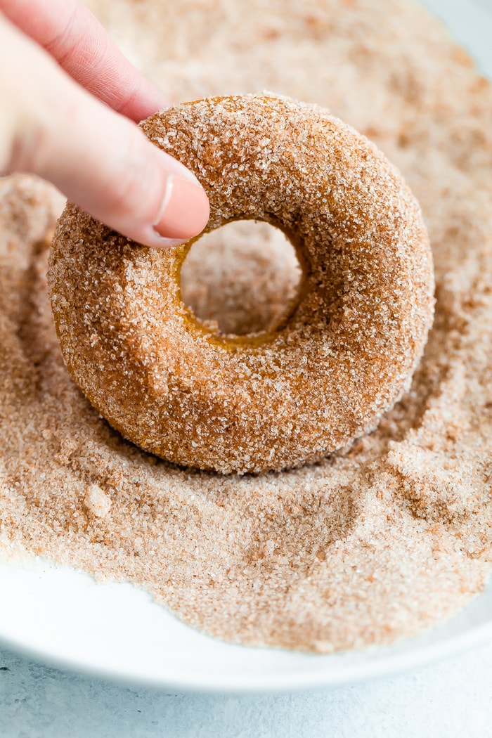 Hand dipping an apple cider donut into cinnamon sugar.