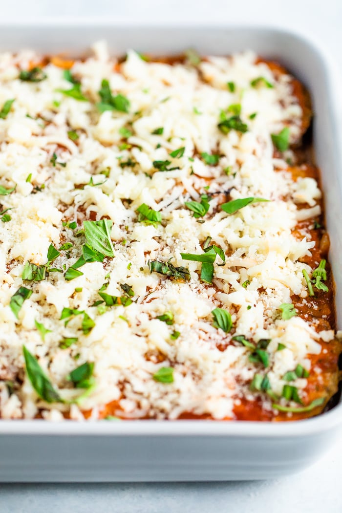 Casserole dish of eggplant parmesan topped with cheese and basil before being baked.