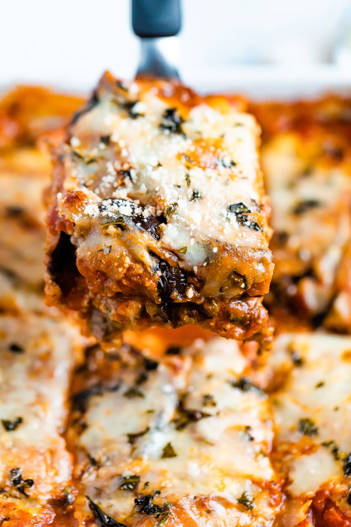 Spatula lifting a slice of eggplant parmesan from a casserole dish.