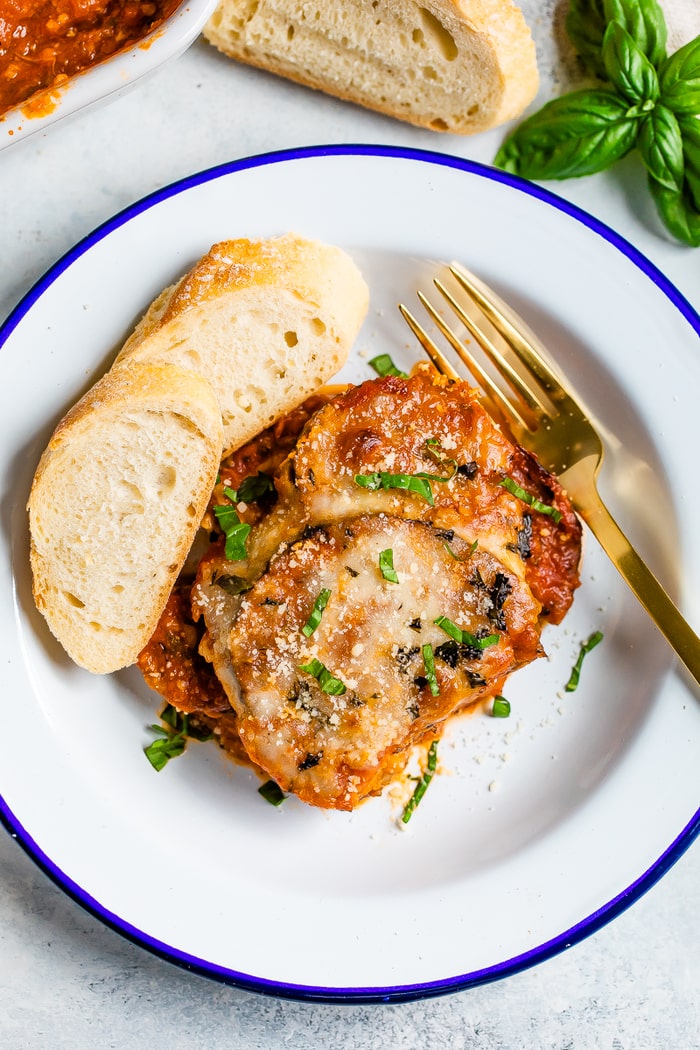 Eggplant parmesan on a plate with slices of bread.