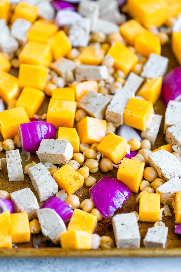 Uncooked chunks of butternut squash, tofu, chickpeas, and onions on a sheet pan.