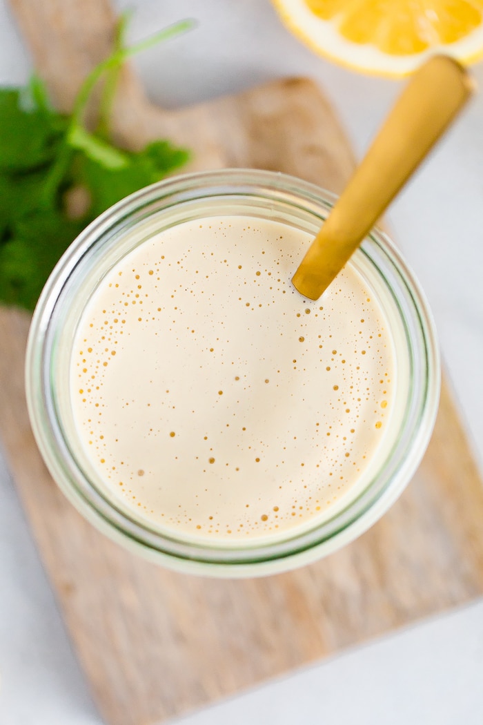 Bird's eye view of a jar with tahini sauce with a gold spoon in the jar.