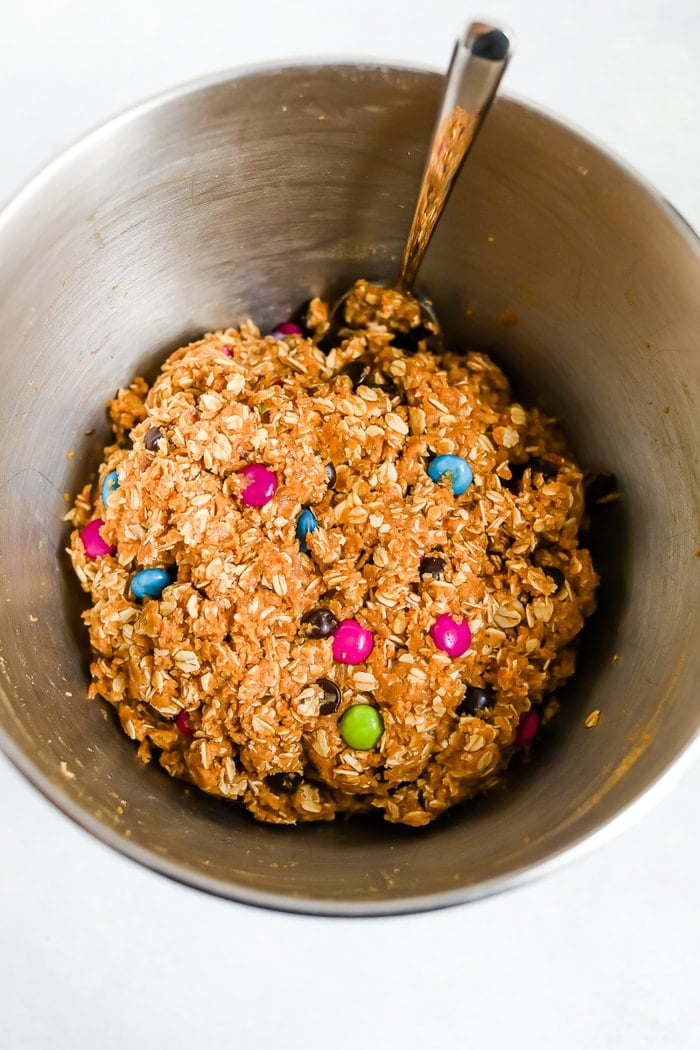 Mixing bowl with cookie dough for gluten-free peanut butter monster cookies. Oats and M&Ms are in the batter.