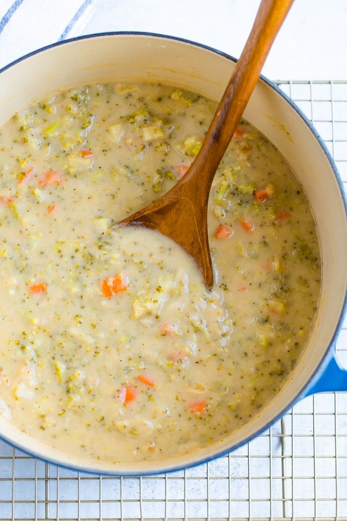 Dutch oven with broccoli cheddar soup and a wood spoon stirring.