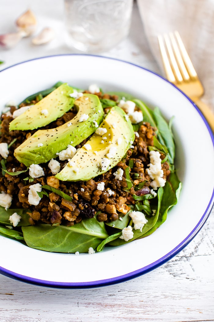 Plate with a bed of fresh spinach topped with a warm Mediterranean salad, topped with feta and avocado.