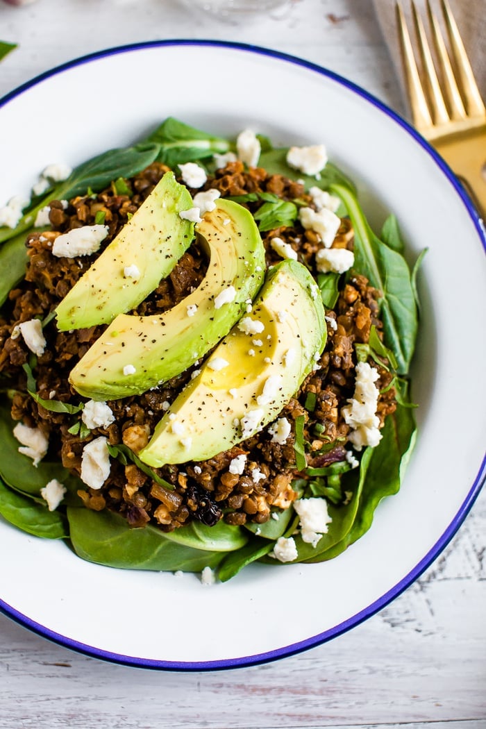 Plate with a bed of fresh spinach topped with a warm Mediterranean salad, topped with feta and avocado.