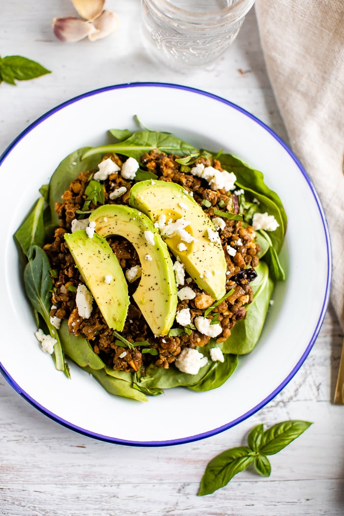 Plate with a bed of fresh spinach topped with a warm Mediterranean salad, topped with feta and avocado.