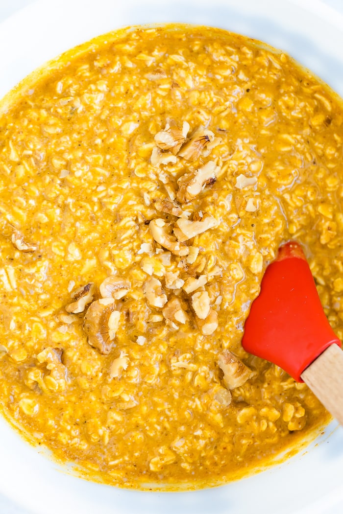 Mixing bowl with batter for the pumpkin baked oatmeal. The mixture is pumpkin, almond milk, walnuts and old fashioned oats. Batter is getting mixed with a spatula.