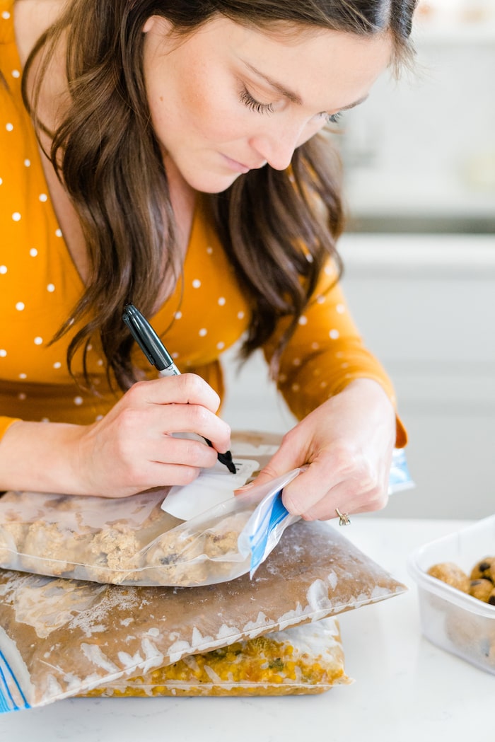 Pregnant woman labeling freezer bag for frozen meals prepped before the baby arrives. 