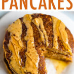 Stack of pumpkin pancakes, drizzled with peanut butter and maple syrup, with a bite taken out of the stack.