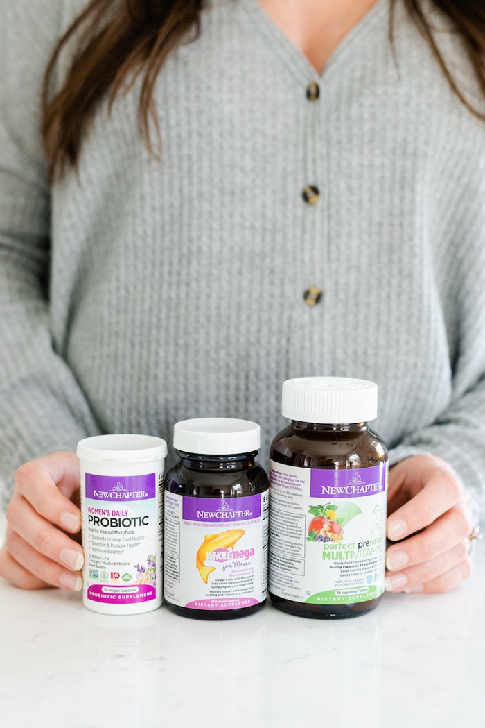 Pregnant woman holding three bottles of New Chapter supplements for pregnancy.
