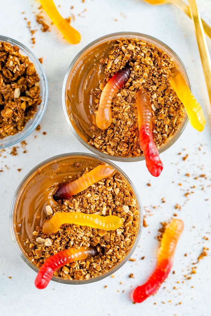 Two dirt pudding cups topped with granola and gummy worms.