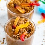 Two dirt pudding cups topped with granola and gummy worms.